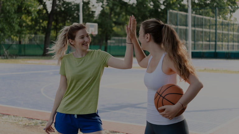 Two women on a basketball court giving each other a high-five.